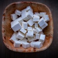 Top view of fresh feta cheese cubes in a rustic wooden bowl, showcasing clean and minimal food photography.