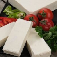 Assorted vegetables and white cheese on a wooden table, ideal for culinary themes.