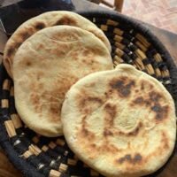 Three freshly baked flatbreads served on a woven basket, perfect for a rustic breakfast.