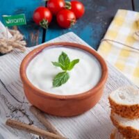 Authentic Turkish yogurt served in a clay bowl with mint, tomatoes, and sesame bread on rustic wooden board.