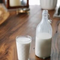 Ornamental glass near transparent bottle of creamy milk on table at home in daylight
